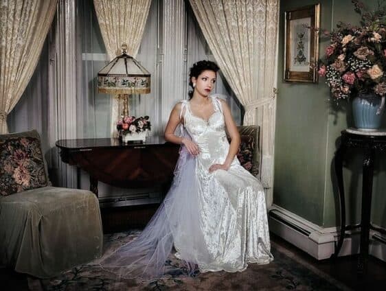 A woman in a vintage wedding dress sits elegantly in a tastefully decorated vintage room.