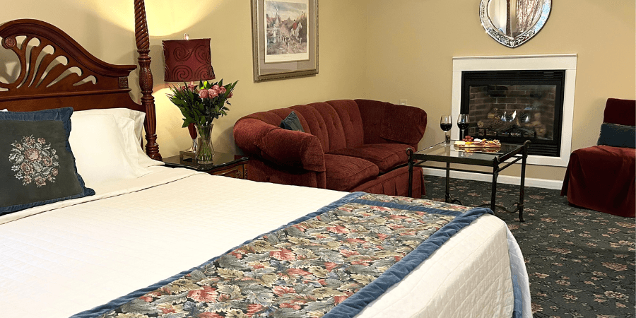 A cozy hotel room featuring a bed, fireplace, and a comfortable seating area with flowers and wine.