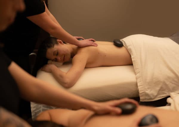 Two women receive hot stone massages in a serene spa setting.