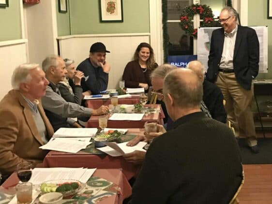 A group of people seated around a table engaged in a discussion during a meeting in a cozy setting.